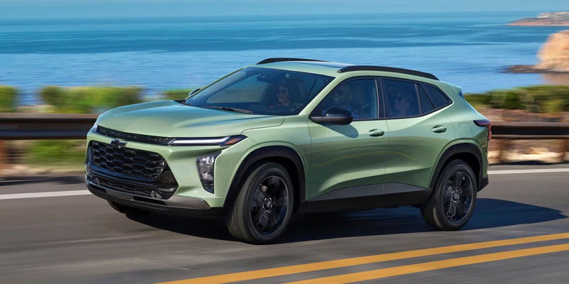 Light green Chevy Trax SUV driving left on a highway, ocean and cliffs in the background